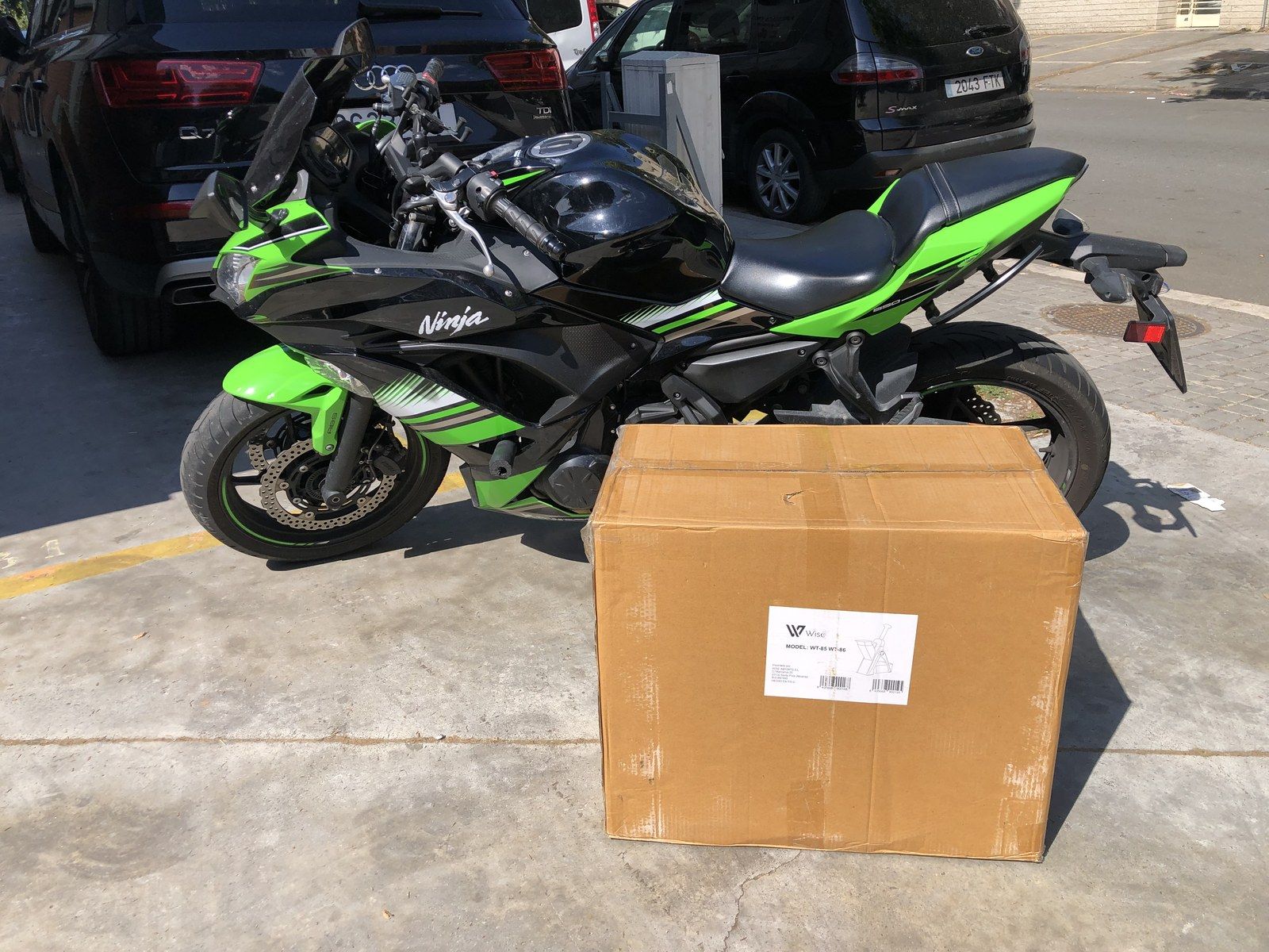 Moto Kawasaki Ninja verde aparcada junto a una caja de cartón con pedidos