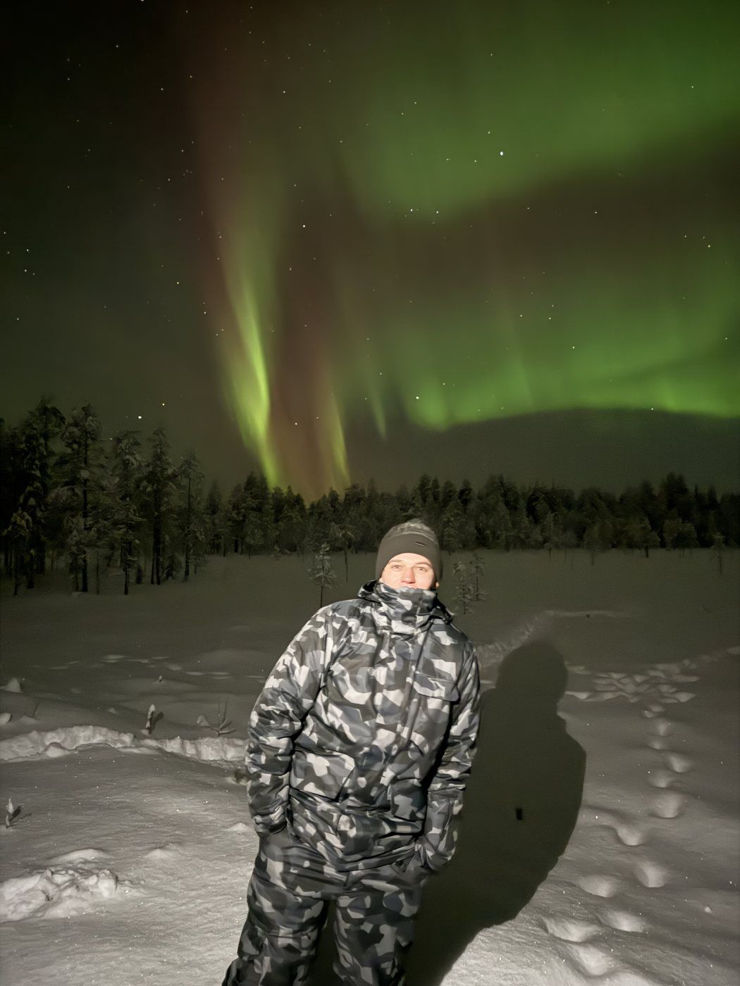 Taras de pie en la nieve bajo una aurora boreal verde